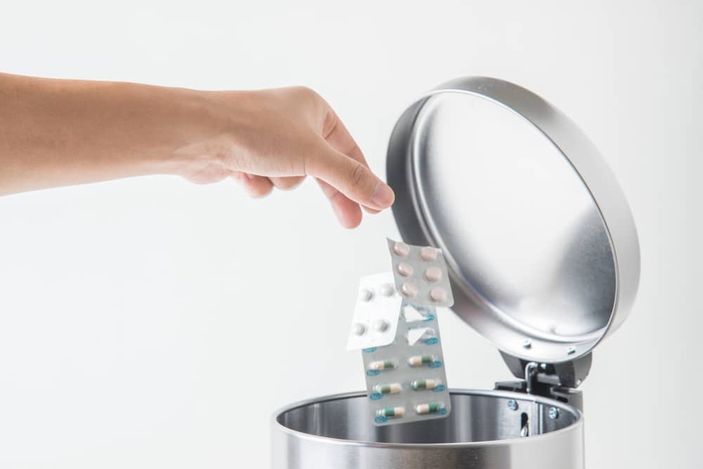 Hand throwing medicine in garbage can.