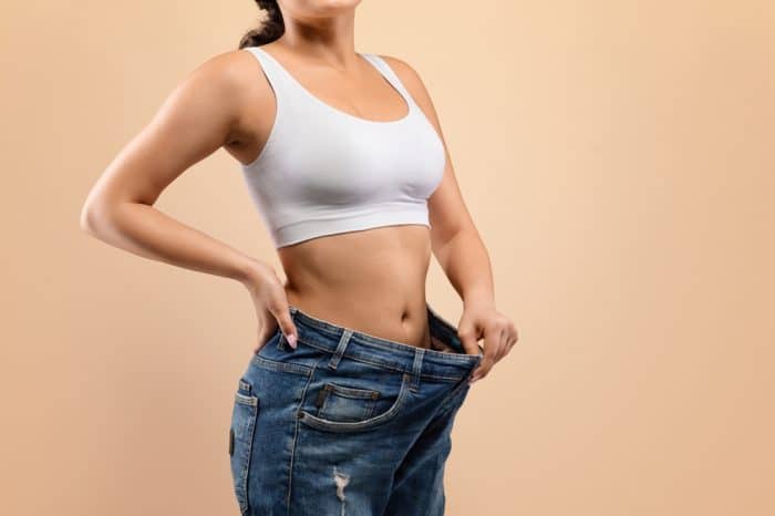 Fit woman holding here loose jeans by the waistband.